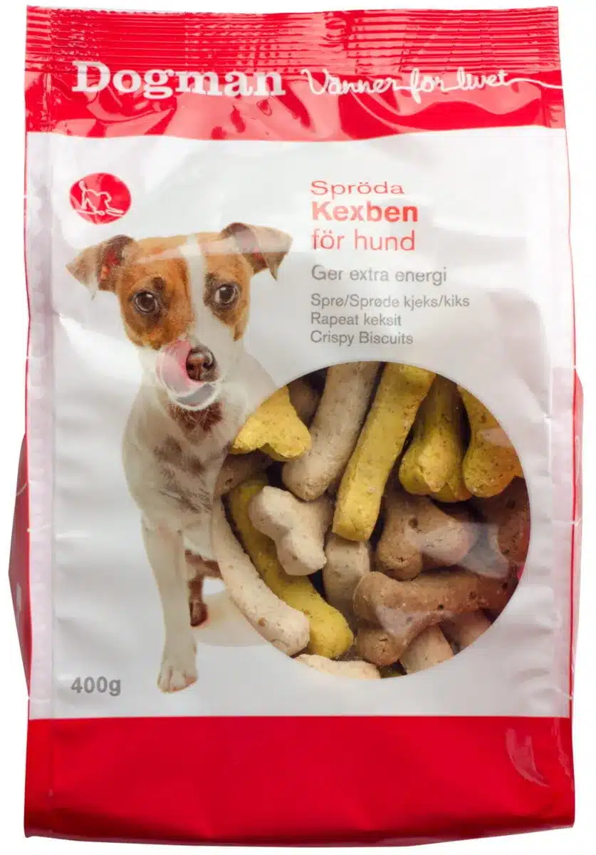 En röd och vit påse med Dogman krispiga kex för hundar har en liten brun och vit hund på framsidan. Påsen framhäver "Spreoda Kexben för hund" och innehåller benformade kex i olika färger, bland annat vitt, gult och brunt. 400 g. Perfekt för alla petzi- eller hundentusiaster.