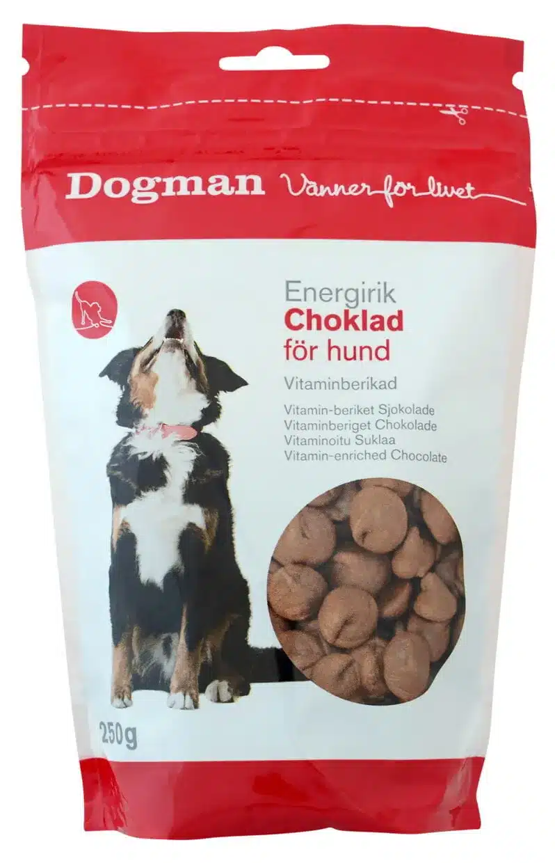 En röd och vit förpackning av "Dogman Vänner för livet" Energirik Choklad för hund, med chokladgodis för hundar. Förpackningen visar en glad hund och innehåller 250g vitaminberikade chokladgodis för hundar.