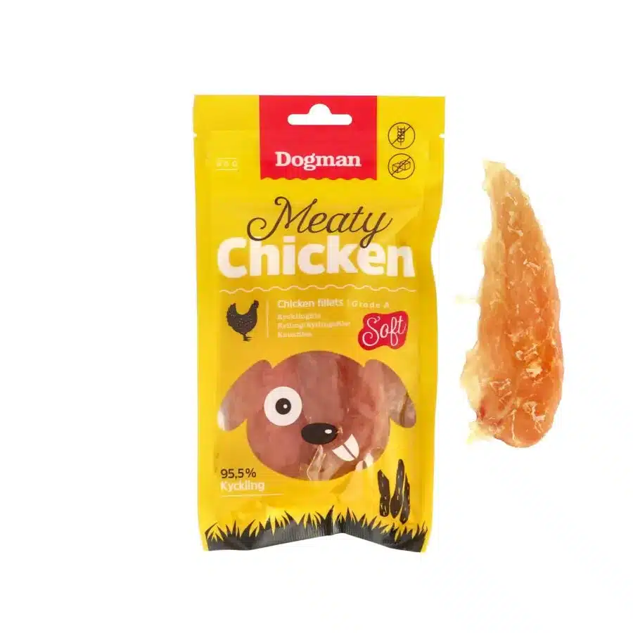 Ett gult paket Dogman Meaty Chicken filéer, med en illustration av en tecknad brun hund på framsidan. Bredvid paketet finns en riktig kycklingfilé som visar produktinnehållet. I paketet nämns "Soft" och "95,5% Kyckling".