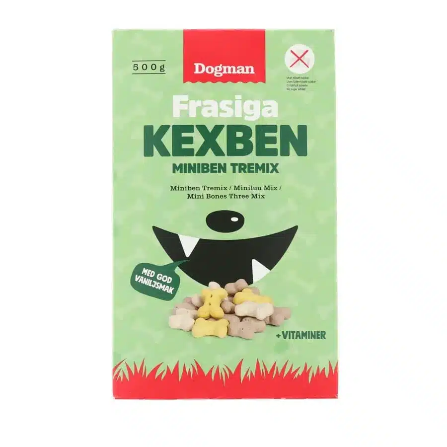 Bilden visar ett grönt och rött paket av Dogman märket "Frasiga Kexben Miniben Tremix" hundgodis. Förpackningen har en illustration av en svart hunds mun och näsa, och olika benformade godsaker syns längst ner. Text indikerar vaniljsmak med tillsatta vitaminer.