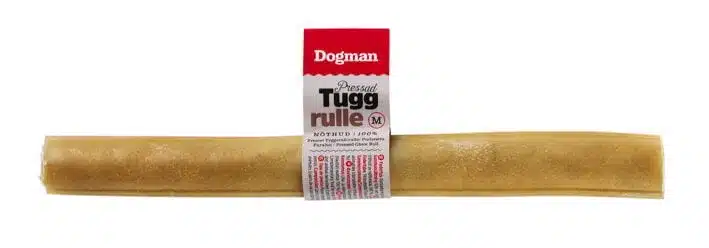 En lång, cylindrisk hundtugg märkt "Dogman Pressad Tuggrulle" med en tagg som visar produktinformation, inklusive en medelstor indikator. Tuggbenet ser ut att vara ljusbrunt och är avsett för husdjur.