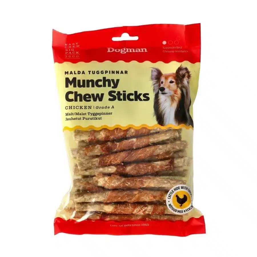 Ett paket Dogman Munchy Chew Sticks för hundar, kyckling smak. Framsidan av den röda och genomskinliga väskan visar en liten Papillon med vit och brun päls. Tuggpinnarna är synliga inuti och texten är på flera språk. Perfekt för din hunds njutning!