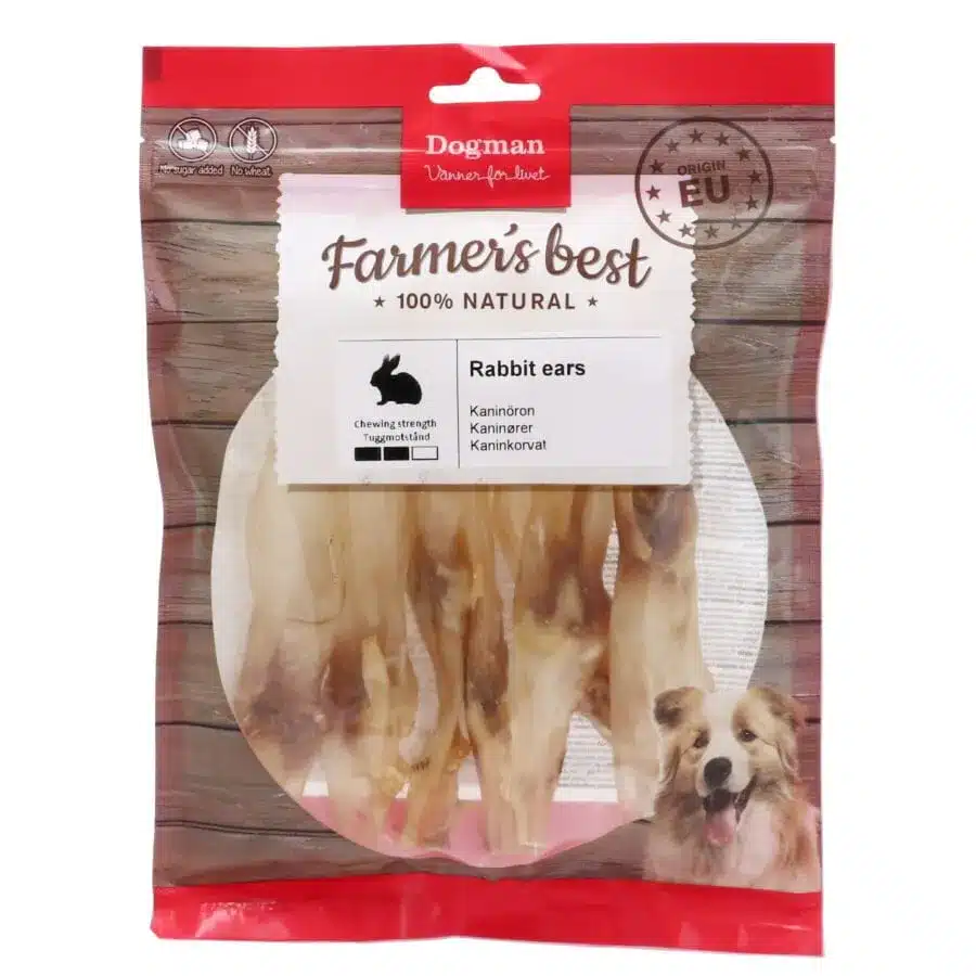 Ett paket med Dogman Farmer's Best 100% Natural Rabbit Ears hundtugg. Förpackningen har ett tydligt fönster som visar kaninöronen inuti, en röd toppremsa med Dogman-loggan och en illustration av en leende hund i det nedre högra hörnet.